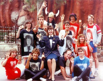 Disneyland Entertainment Art Department, "DEAD" 1989 Canoe Team posing for a photo. Wendy Freeland, Disneyland Ambassador to the World sits in the middle. Everyone else wears t-shirts with giant halftone dot photos of Wendy in red, blue, or black